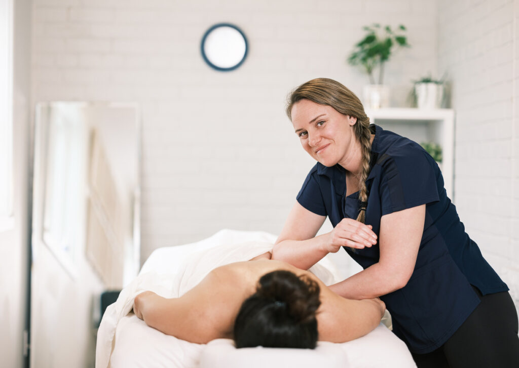A registered massage therapist (RMT) smiling as she treats a client.